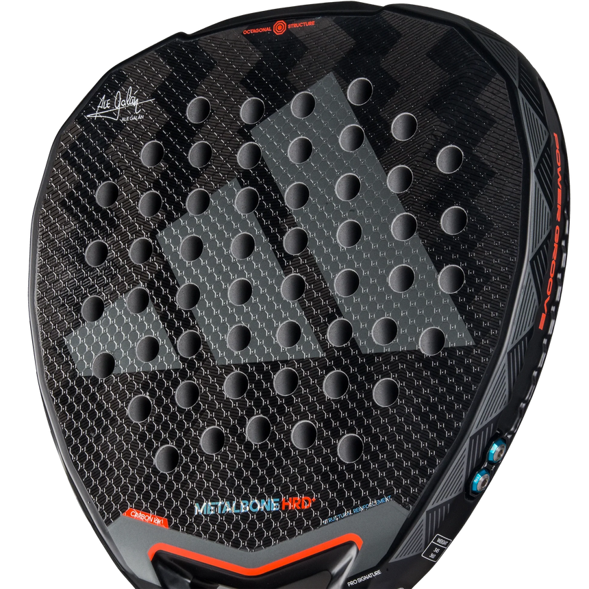 A close-up of the Adidas Metalbone HRD+ 3.4 Ale Galan 2025 padel racket reveals its textured surface with circular holes, designed for offensive players. Red and blue accents border the METALBONE HRD print, emphasizing its customizability. The handle is partially visible at the bottom.