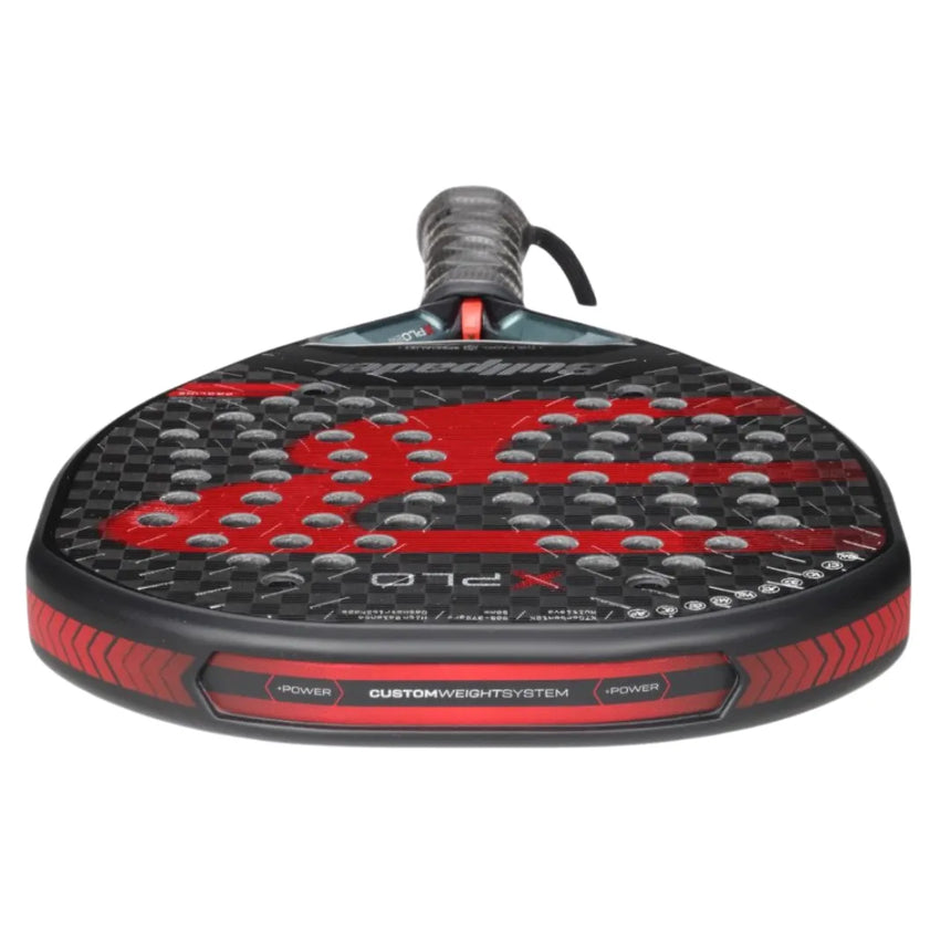 A close-up of the black and red BULLPADEL RACKET XPLO 2025 MARTÍN DI NENNO for advanced players showcases a textured surface with circular holes. It features a CUSTOM WEIGHT SYSTEM at the handles base, with bold lines and patterns that reflect BullPadels signature style.