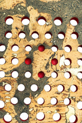 The Cork Padel Extreme Red by Cork Padel features a limited edition design with a textured surface and irregular circular cutouts. Some circles contain red spheres, set against a beige and dark swirled pattern resembling wood grain or marble.