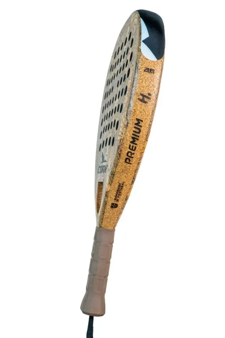 The Cork Padel Premium Hybrid III Racket features a textured surface and multi-diameter hole pattern for precision, an advanced anti-vibration cap, and a firm grip in light brown with brand markings and the word Premium.