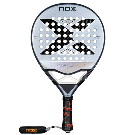 The Nox Padel Racket AT Pro Cup Comfort 25 by Agustín Tapia features a gray and black design with a large X and multiple holes. It uses Fiber Glass Silver construction, has a black grip with NOX in orange, and includes a wrist strap for comfort.