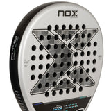 A close-up of the NOX Padel Racket AT10 Genius 18K by Agustin Tapia 2024 reveals a metallic-finished aluminized carbon fiber construction. It features an X pattern, circular holes, branding text, and subtly integrated EOS Flap technology with technical specs on the frame.