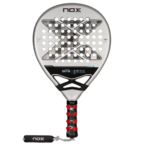 The NOX Padel Racket AT10 Genius 18K by 2024 Agustin Tapia, crafted from aluminized carbon fiber, features a silver design with a black grip and red accents. Its face has a geometric pattern with round holes and NOX displayed top and bottom, enhanced by innovative EOS Flap technology.