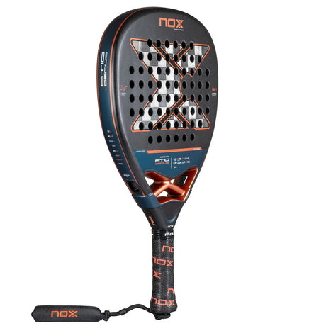 The Nox Padel Racket AT10 Genius Attack 18K Alum 2025 by Agustin Tapia features a perforated black diamond head with orange and blue X accents. Made from 18K carbon for durability, it includes Enhanced Spin Technology, branded text on the frame, and a black grip with orange NOX logos.